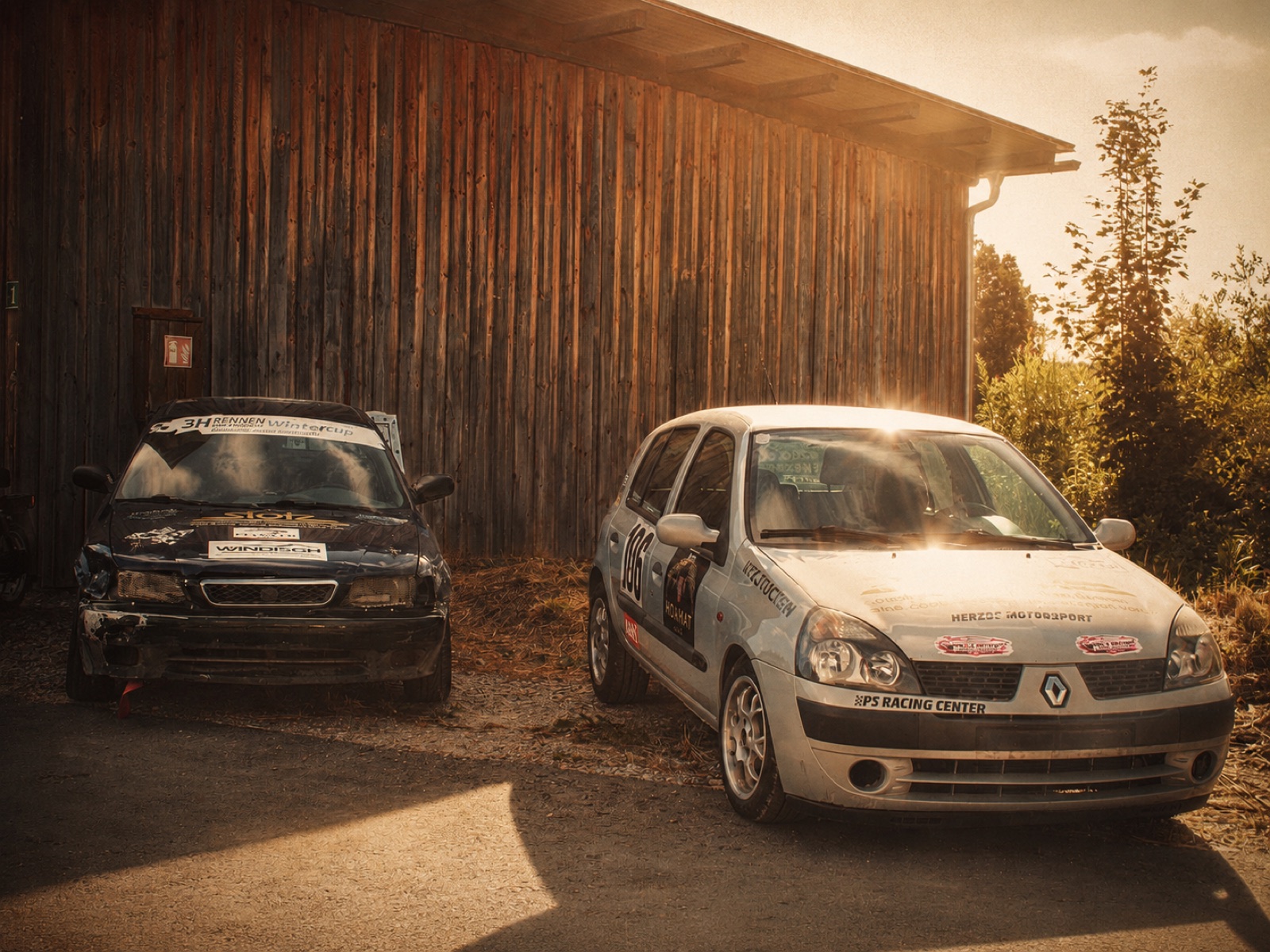 Zwei Motorsportfahrzeuge vor einer Werkstatthalle